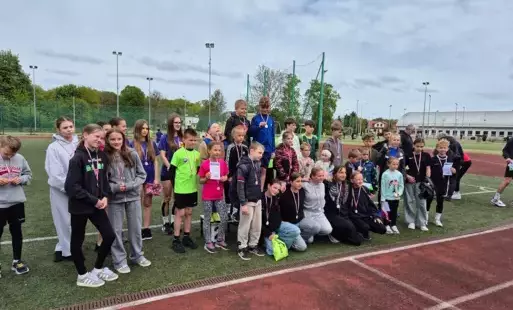 Zdjęcie grupowe zawodników i zawodniczek na tle stadionu lekkoatletycznego